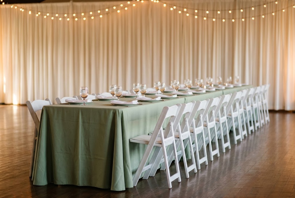 Banquet table seating with white padded folding chairs and sage green linen against a draped backdrop for a San Jose event